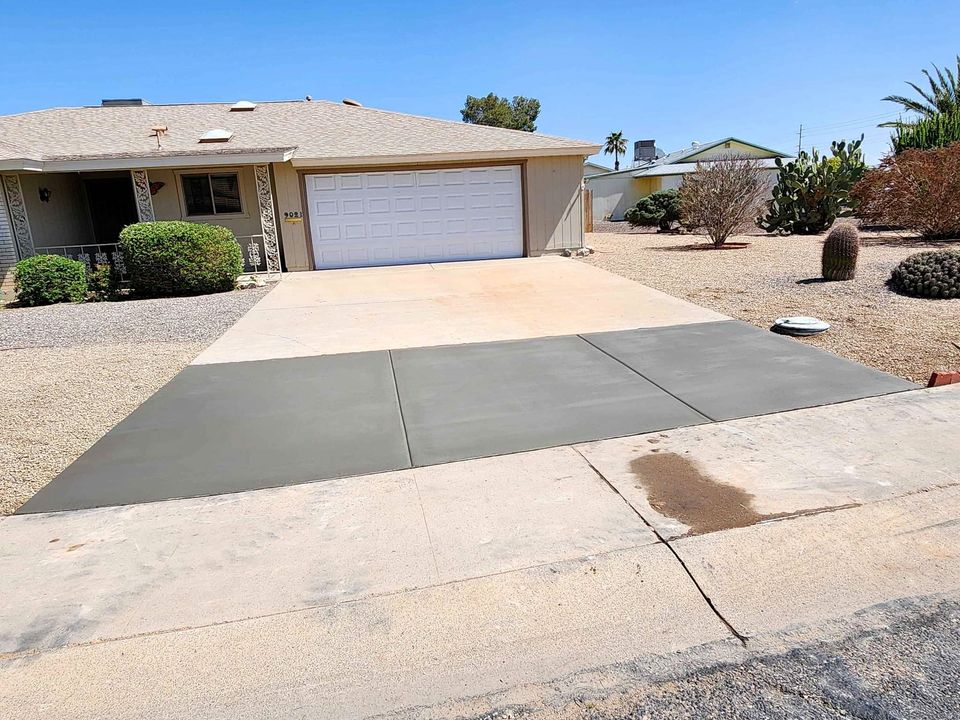 A suburban house in Scottsdale with a two-car garage has a freshly paved concrete driveway, expertly crafted by licensed concrete contractors. The front yard is landscaped with gravel and desert plants. The sky is clear and blue, indicating a sunny day.