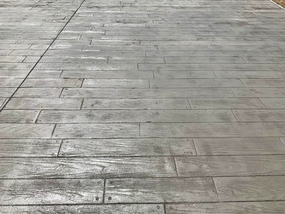 A close-up view of a textured concrete surface designed to resemble wooden planks. The pattern includes linear grooves and nail imprints, enhancing the wood-like appearance. Crafted by Scottscrete Contracting in Scottsdale AZ, this gray concrete driveways installation features subtle variations in shading.