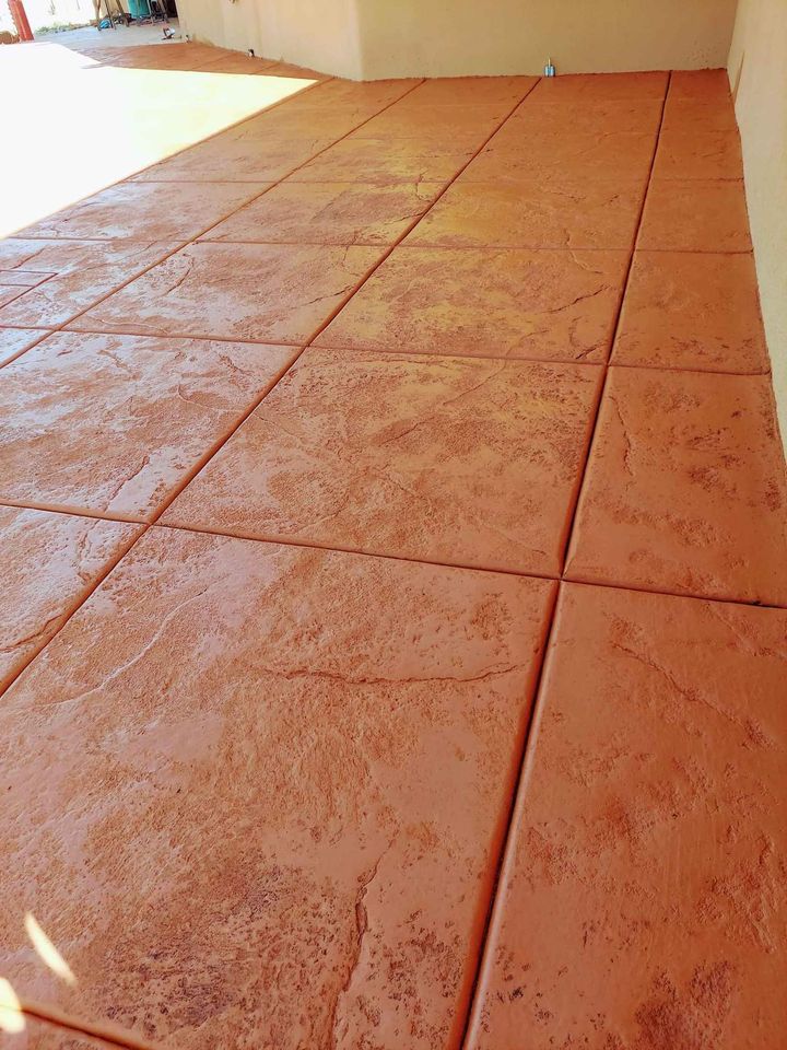 A smooth, reddish-brown concrete patio with decorative, textured square tiles arranged in a grid pattern by Scottscrete Contracting adds a stone-like appearance to the surface. Clean and reflective, it suggests recent construction or renovation—a hallmark of quality work from Scottsdale AZ's finest.